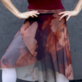 Person wearing a colorful skirt and white tights with ballet shoes on a concrete floor.